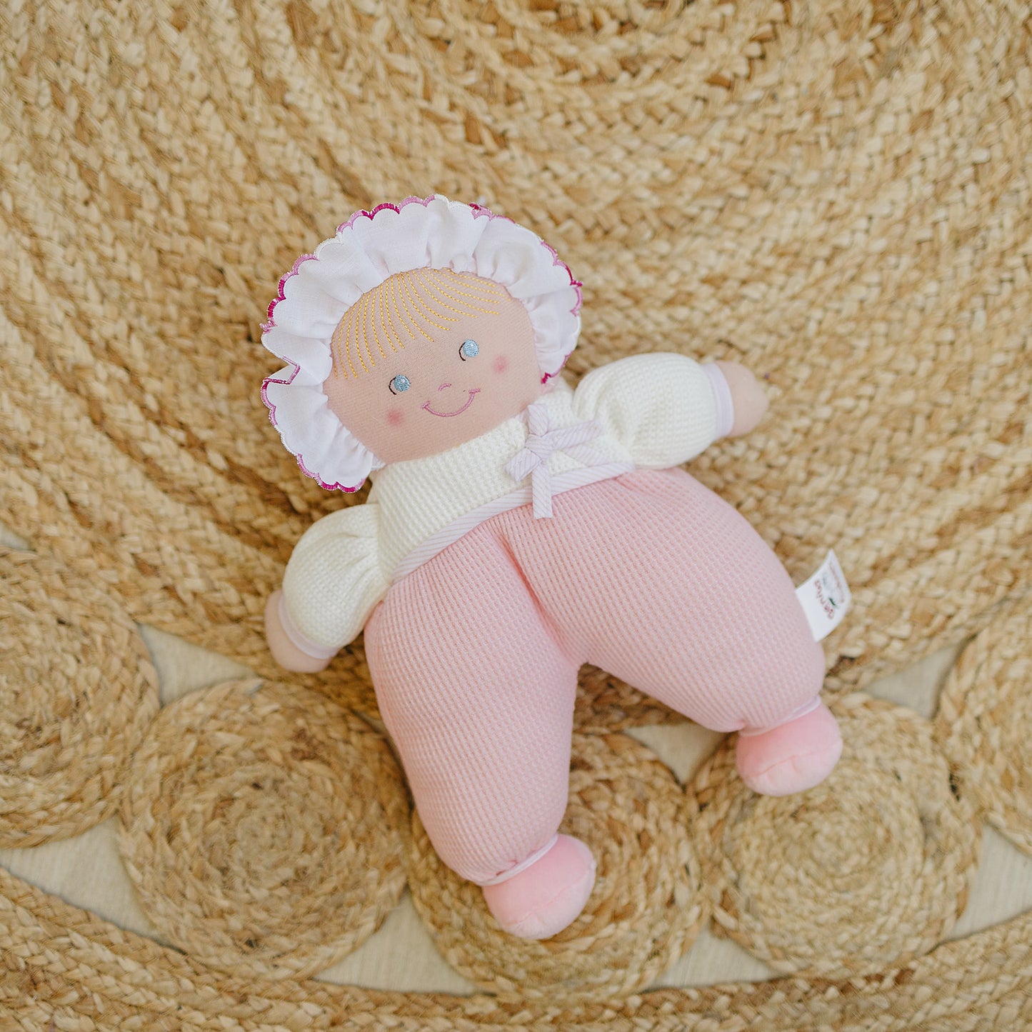 Small doll with a pink outfit and white bonnet on a woven mat